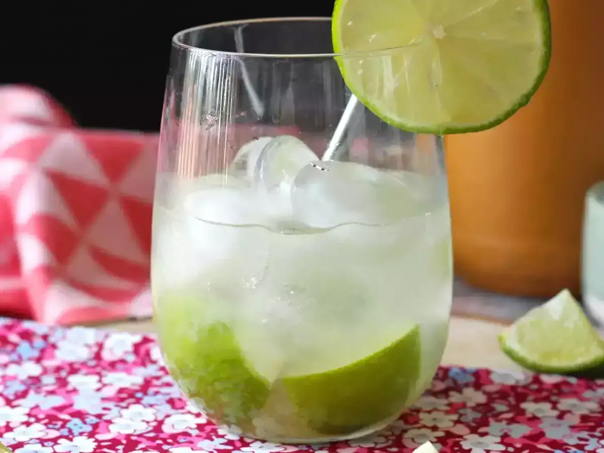 Verre de caipirinha rafraîchissante avec des glaçons, des morceaux de citron vert et une tranche décorative. La recette parfaite pour l'été.