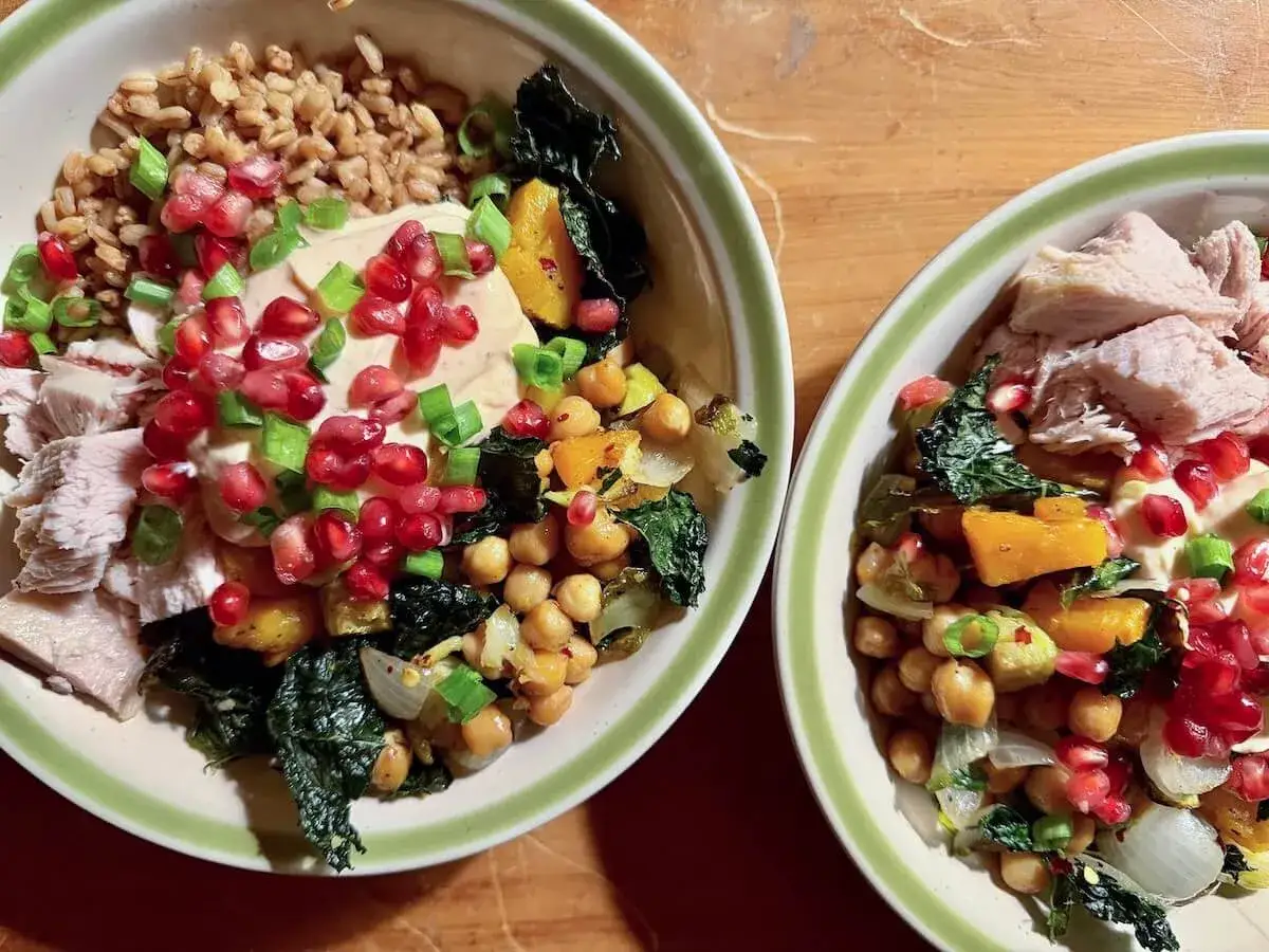 Dos bowls llenos de farro, garbanzos, pavo, calabaza, col rizada y granada. ¡Una comida completa y deliciosa!