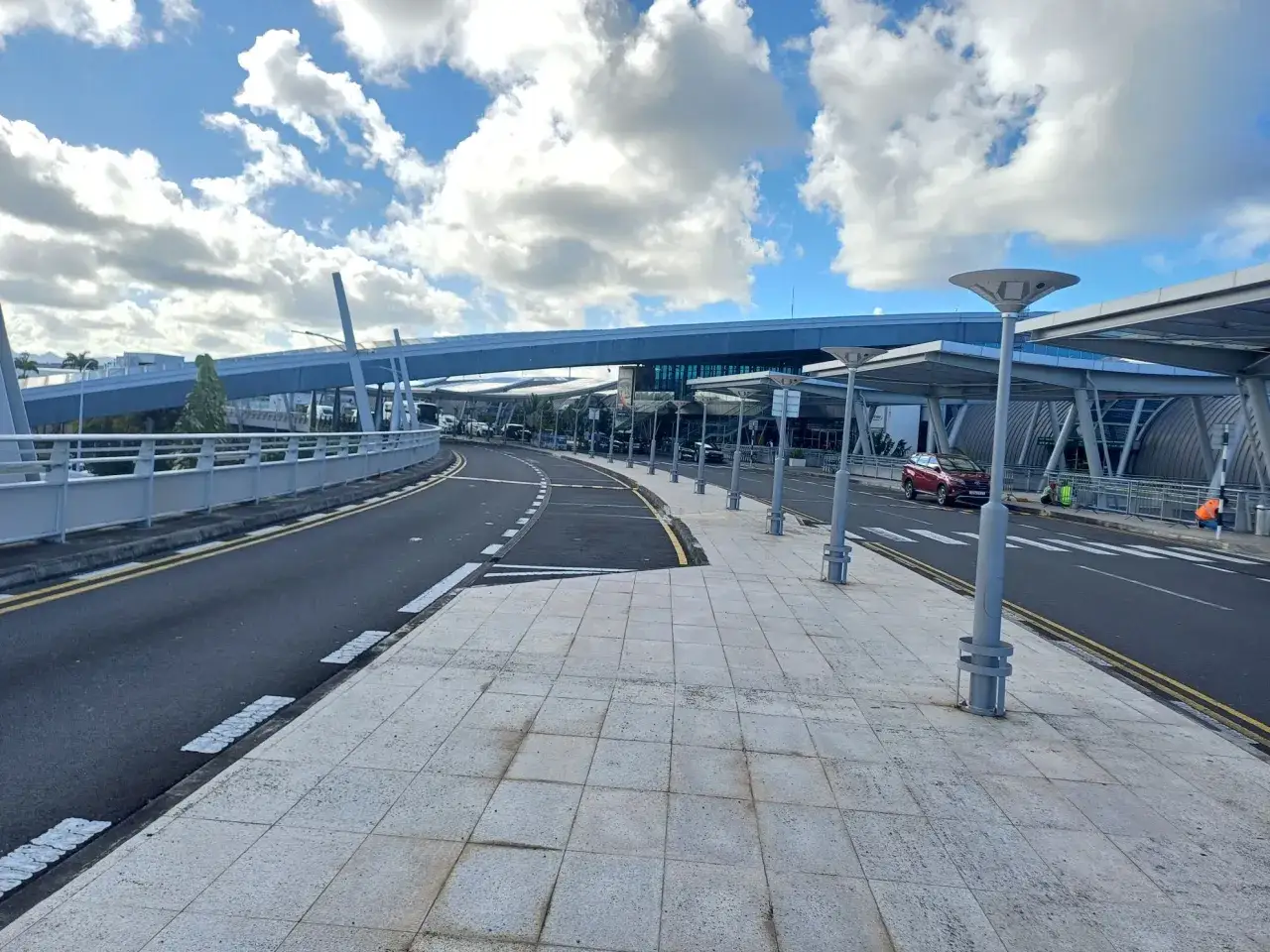 Nowoczesny budynek lotniska na Mauritiusie z podjazdem i chodnikiem. W tle widać samochody i pasażerów.
