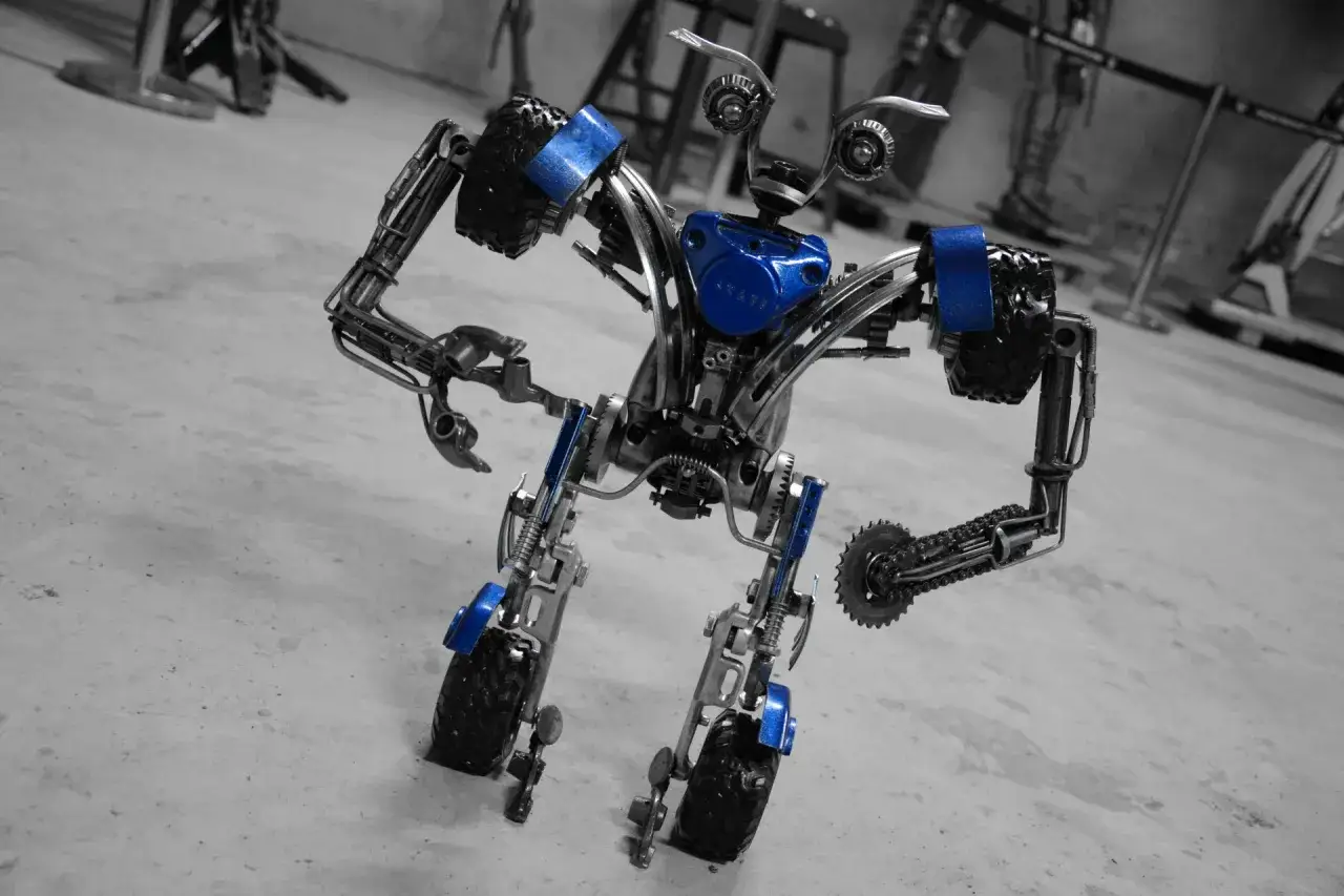 Metalowy robot z niebieskimi akcentami, stojący na betonowej posadzce. To dzieło z fabryki robotów w Mosznej, gotowe do pracy.
