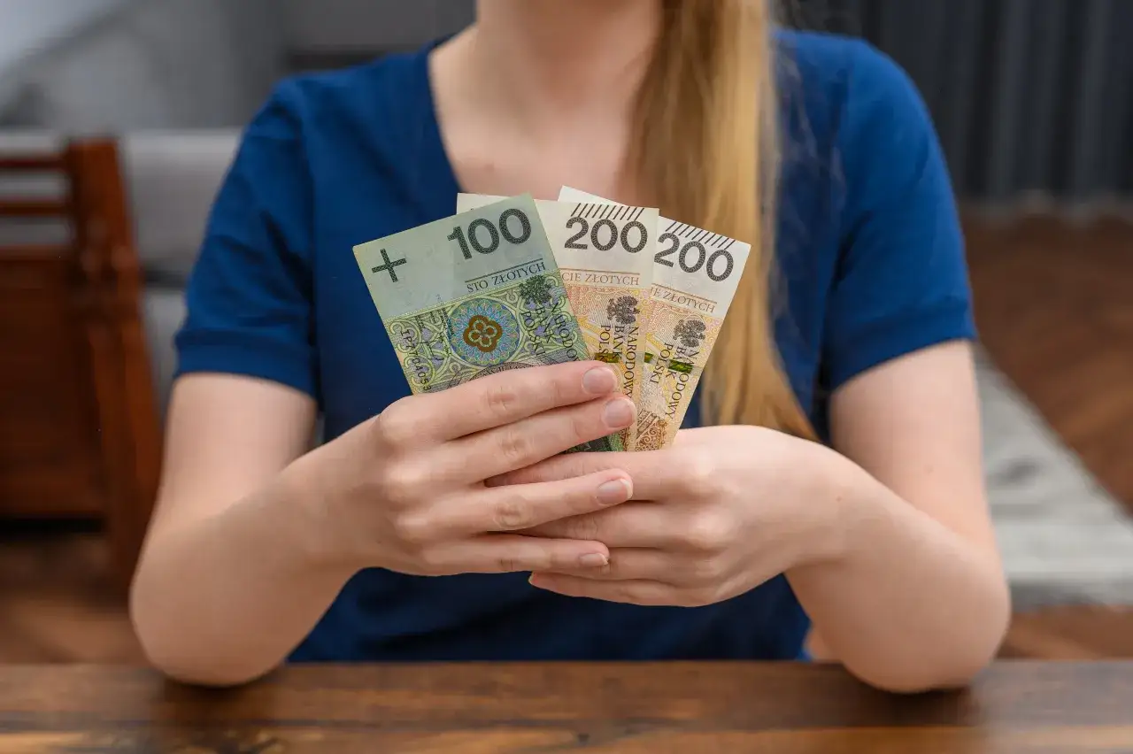 Ręce trzymają polskie banknoty 100 i 200 zł. Konfederacja chce wprowadzenia 
