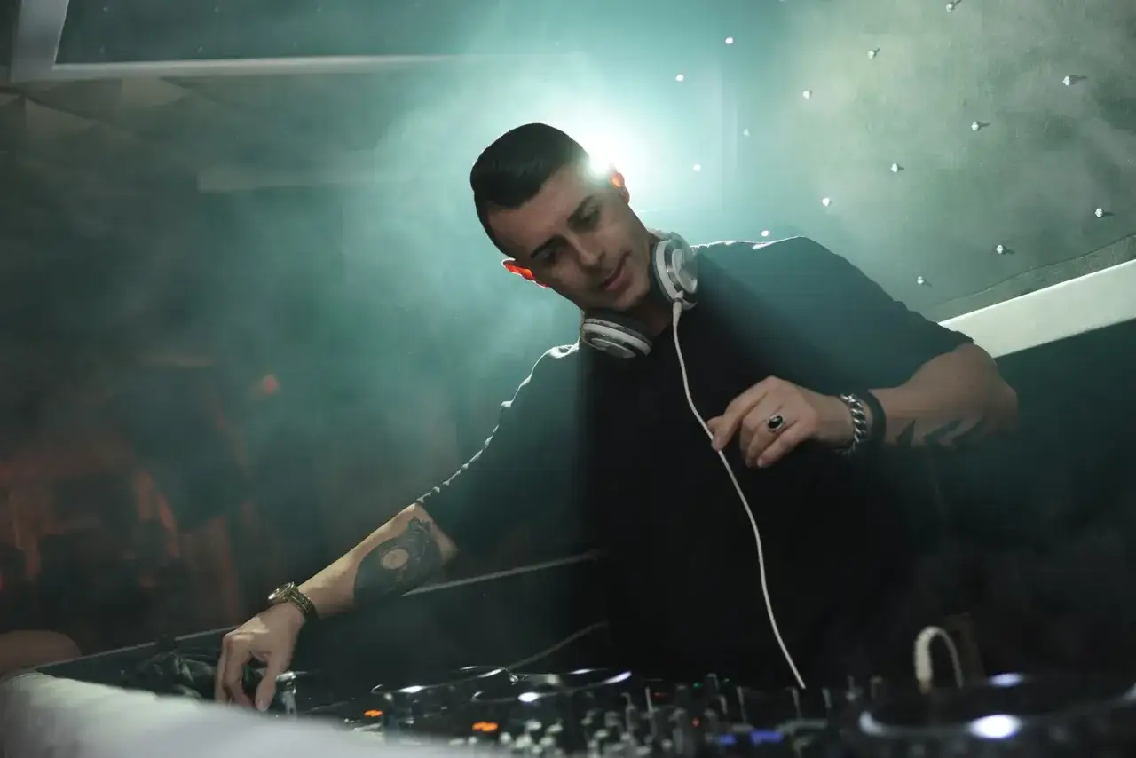 Un artiste deep house mixe dans une ambiance enfum&eacute;e, sous des lumi&egrave;res tamis&eacute;es.