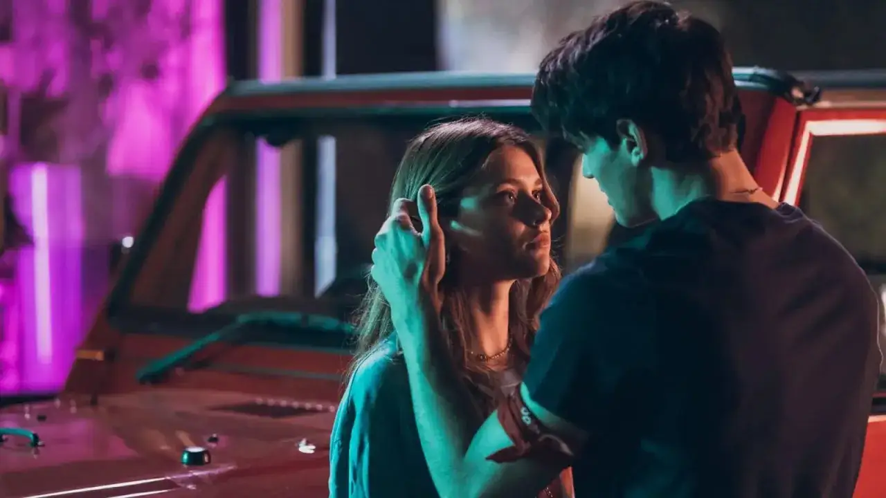 Coppia giovane in un'atmosfera notturna, con luci al neon e un'auto rossa. Scene romantiche e intense, perfette per film simili ad After.