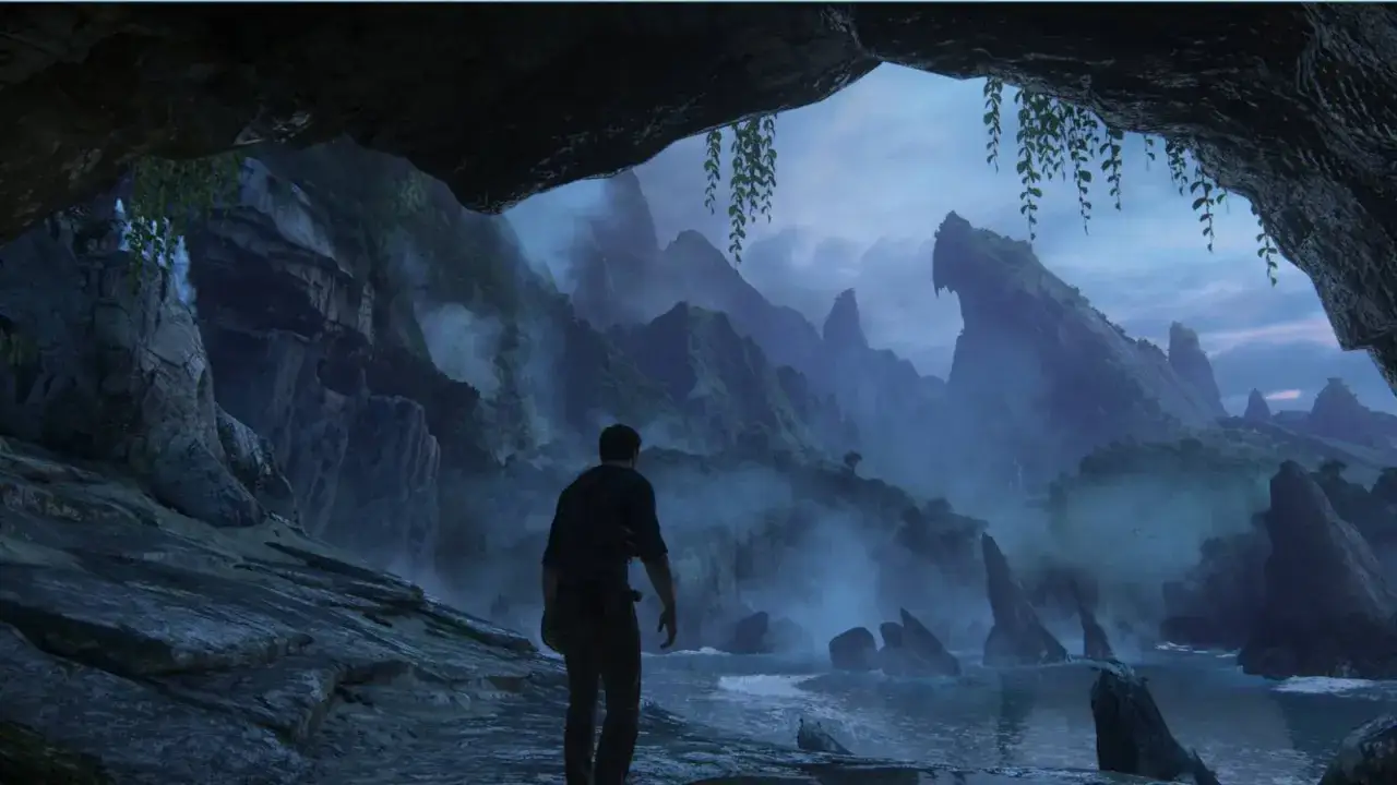 Un aventurero contempla un paisaje brumoso y montañoso desde una cueva, listo para explorar lo desconocido en Uncharted para PC.