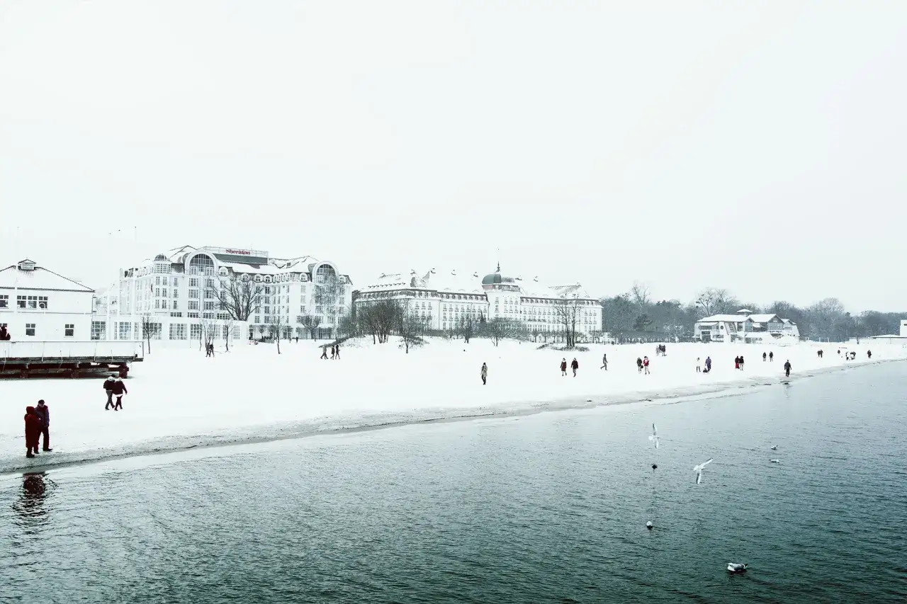 Zimowe Sopot atrakcje: plaża i morze w śnieżnej scenerii, spacerujący ludzie, budynki hotelowe.
