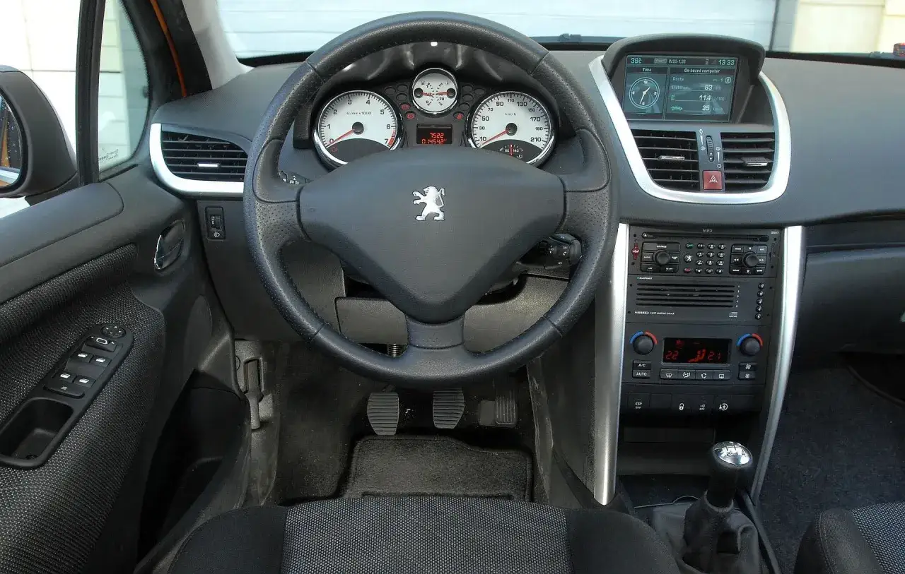 Wnętrze Peugeota 207 1.4 benzyna: kierownica z logo, zegary, ekran komputera pokładowego i radio.