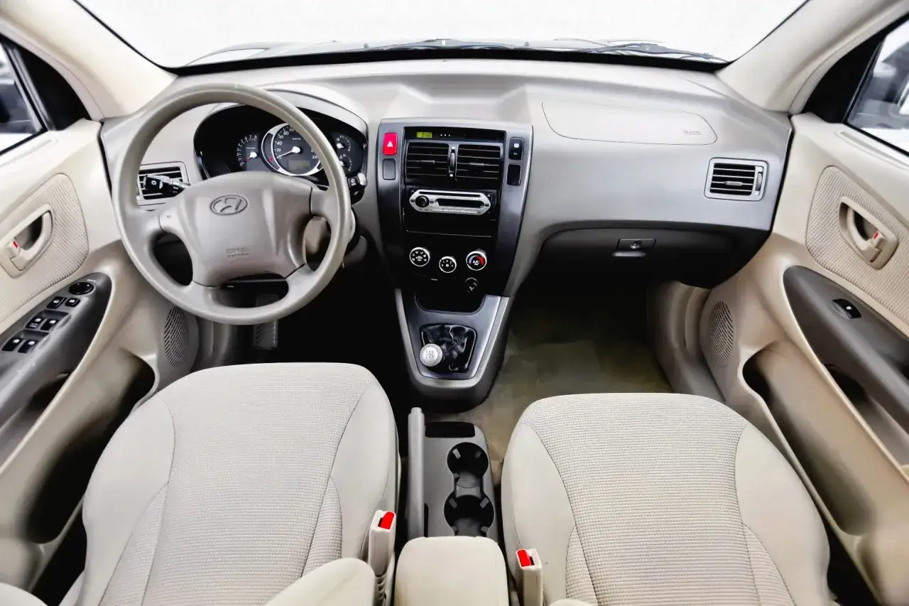 Wnętrze Hyundai Tucson 2007: kierownica, deska rozdzielcza z radiem i nawiewami, dźwignia zmiany biegów, jasne fotele.