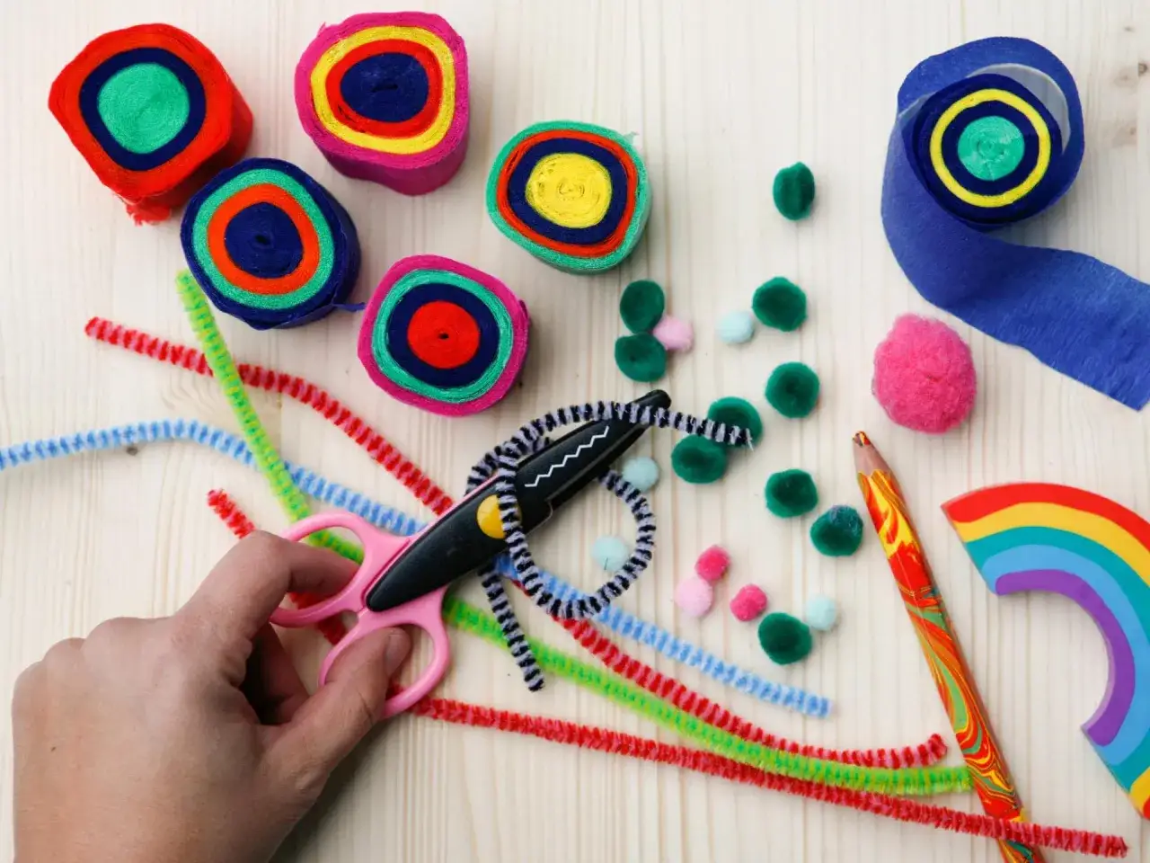 Bunte Papierrollen und Pfeifenreiniger liegen bereit f&uuml;r kreatives Basteln. Eine Hand h&auml;lt eine Schere, um die bunten Dr&auml;hte zu schneiden.