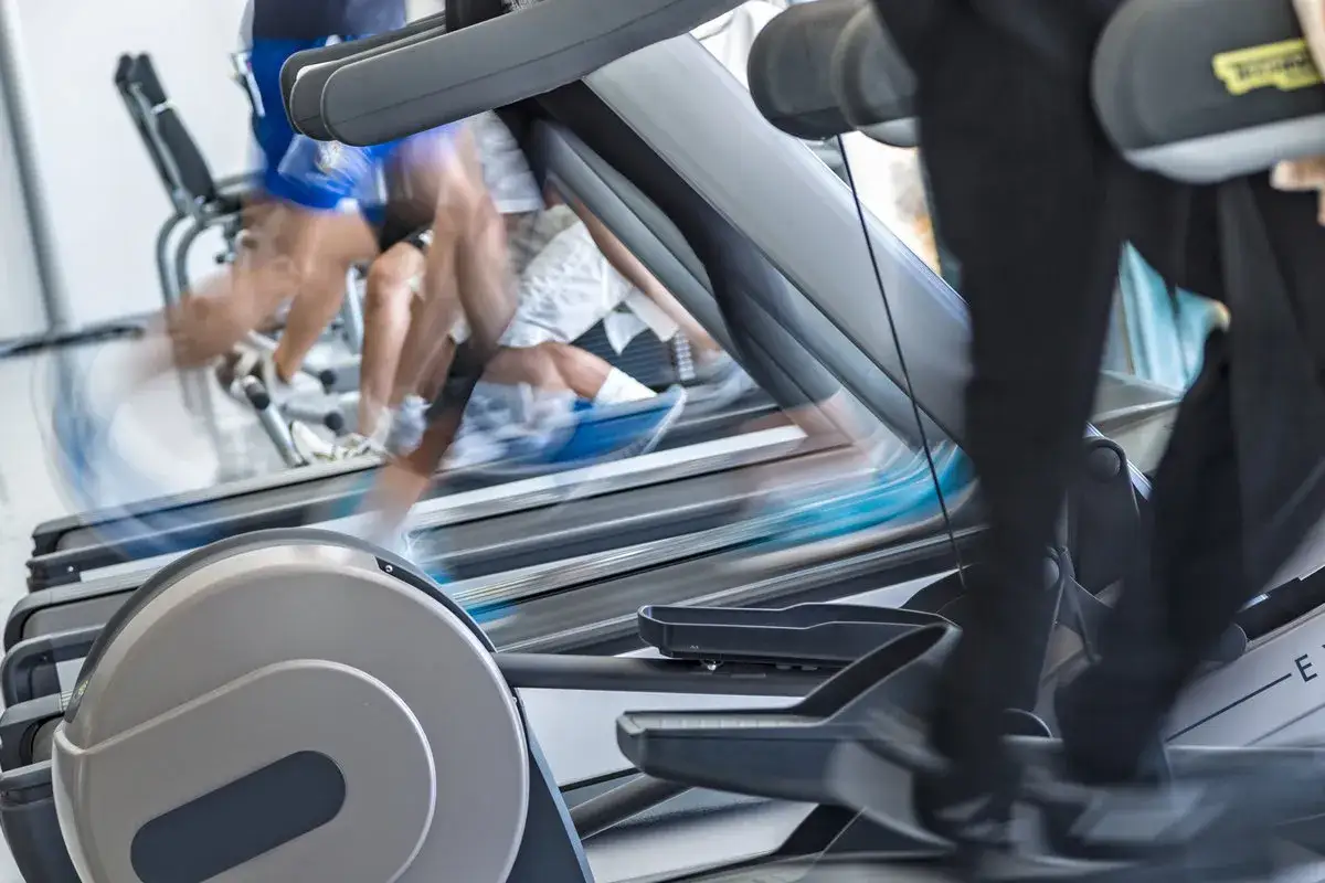 Intensywny trening cardio na siłowni. Rozmyte sylwetki ćwiczących na bieżniach i orbitrekach tworzą dynamiczną atmosferę.