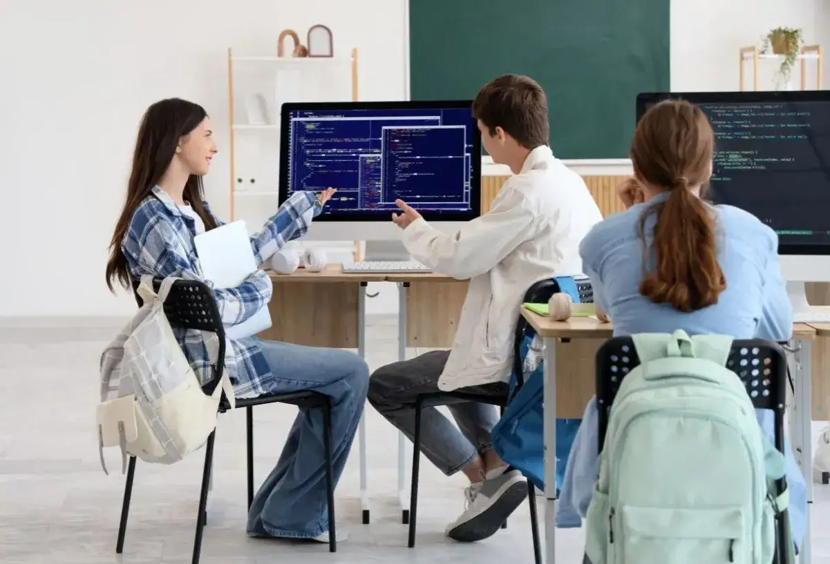 Studenci podczas praktyk programistycznych dyskutują nad kodem na ekranie komputera.