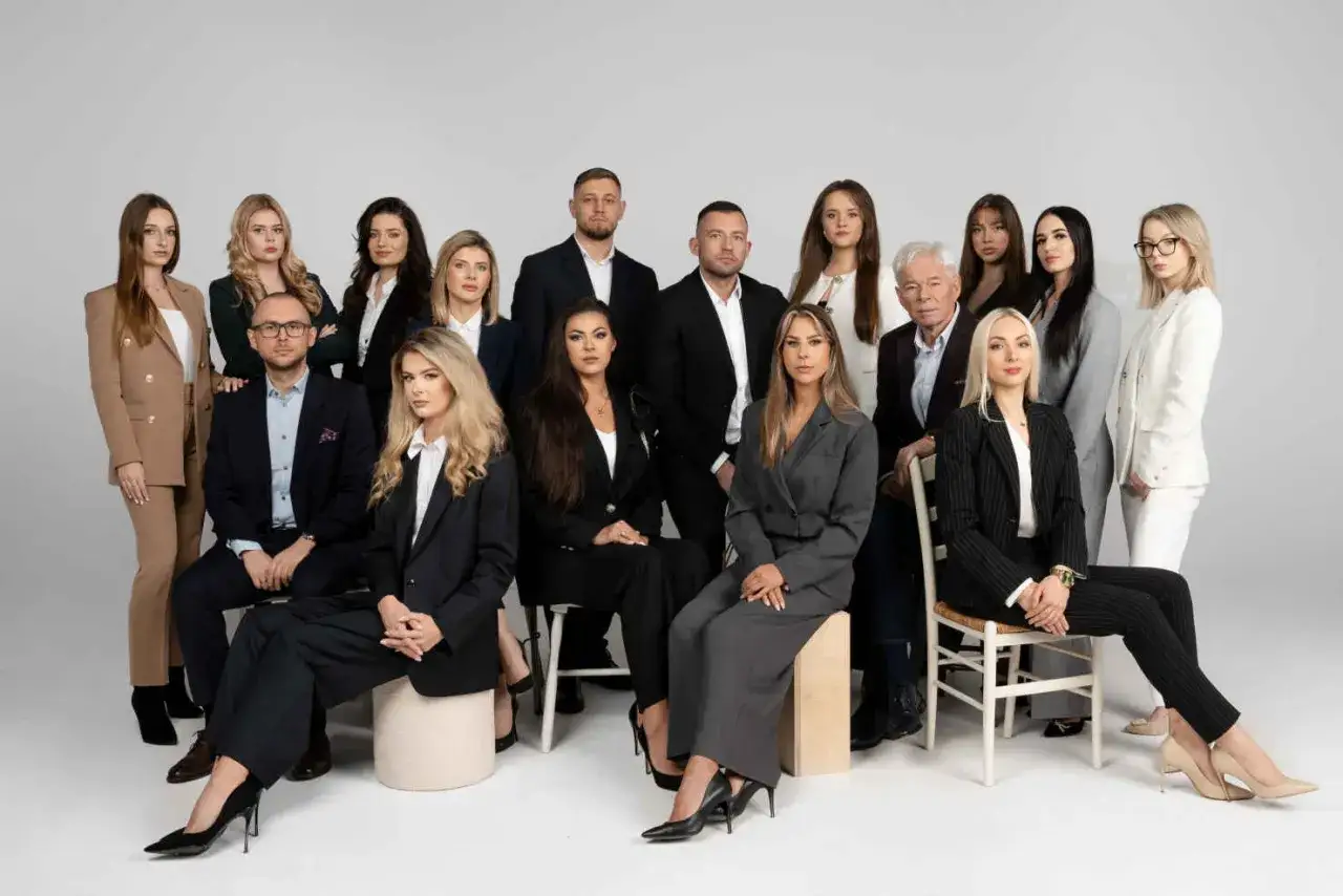 Grupa profesjonalistów w garniturach i kostiumach pozuje do zdjęcia na jasnym tle.
