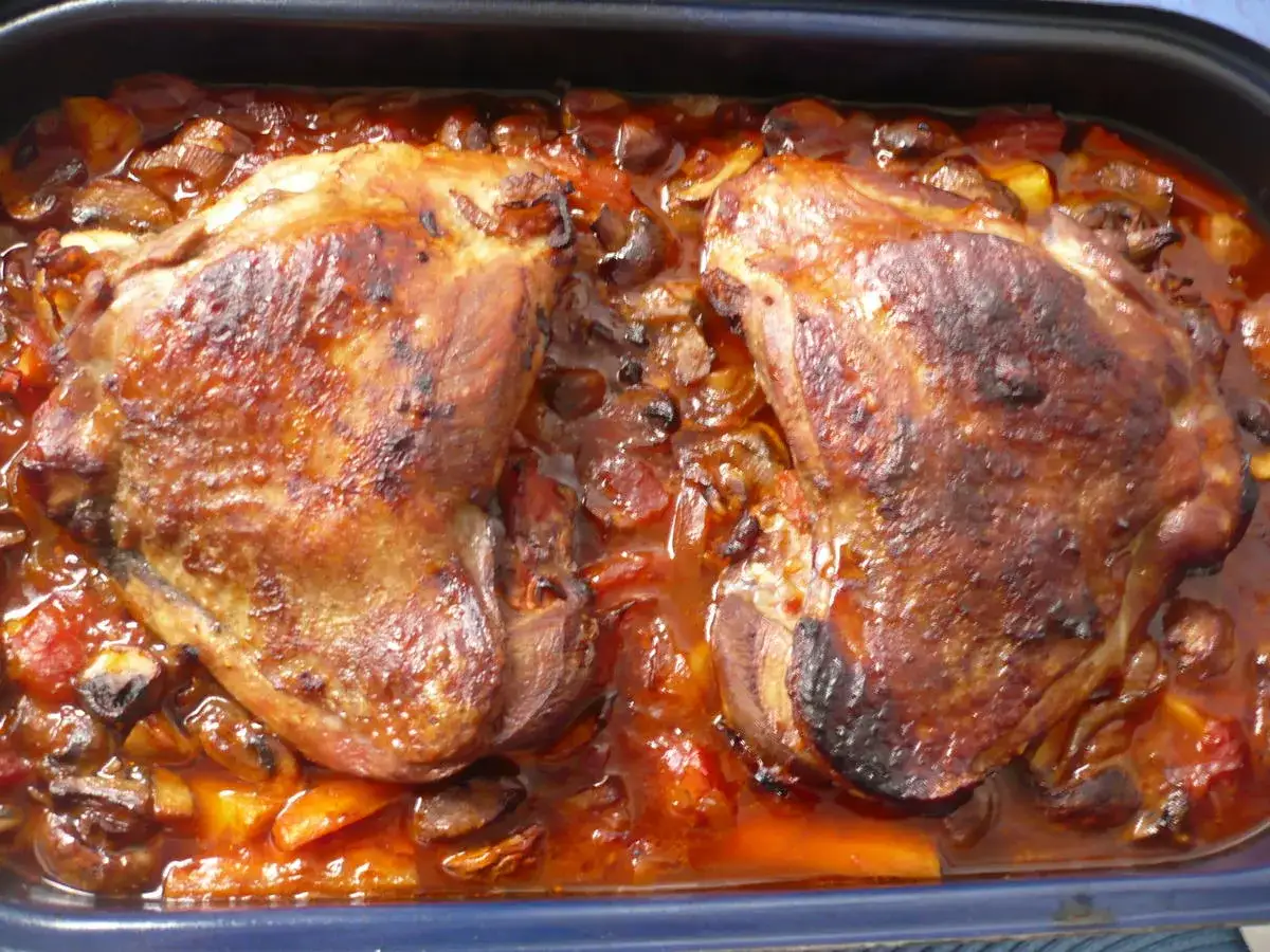 Zwei goldbraune Putenkeulen garen im Ofen in einer aromatischen Sauce mit Gemüse und Pilzen.