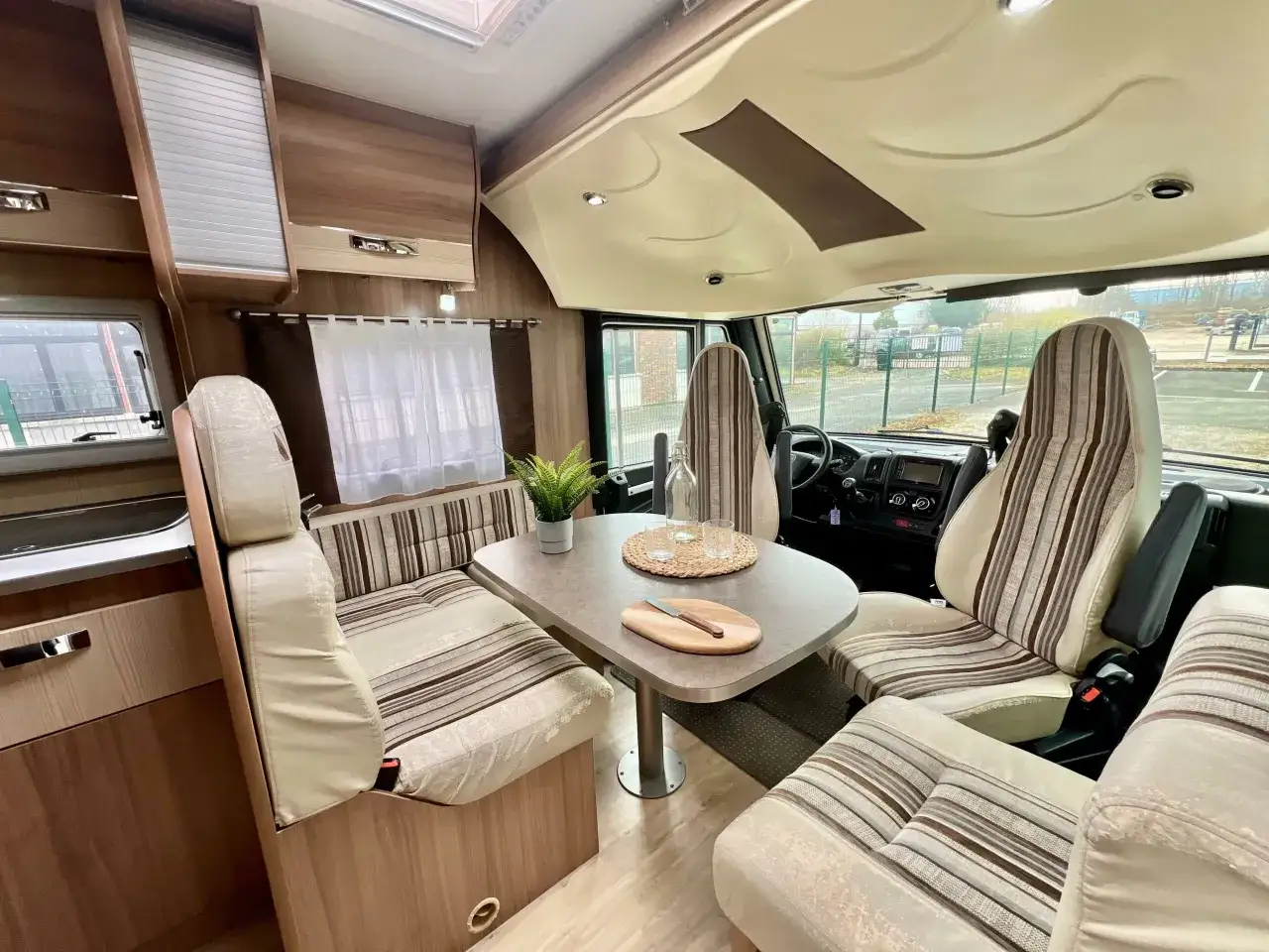 Int&eacute;rieur du camping-car Pilote G740 : salon avec banquettes, table, si&egrave;ges pivotants et cuisine.