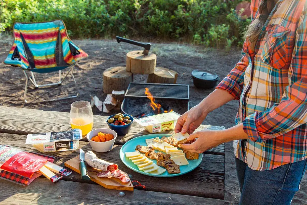 Un délicieux repas randonnée avec fromages, saucisson, olives et fruits secs, près d'un feu de camp.