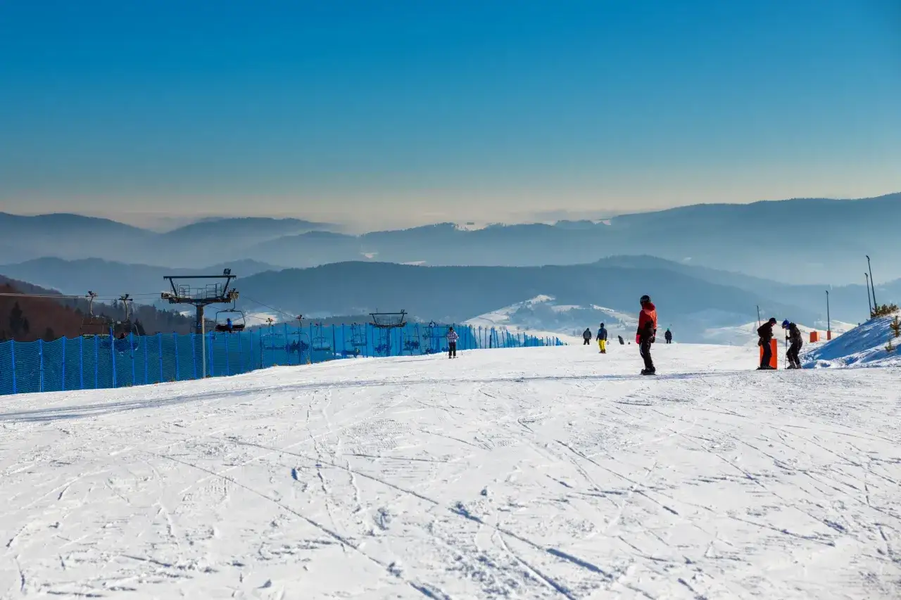 Słoneczny dzień na stoku narciarskim w Małopolsce. Ludzie jeżdżą na nartach i snowboardach, w tle widać wyciąg krzesełkowy i góry. Idealne ferie zimowe!