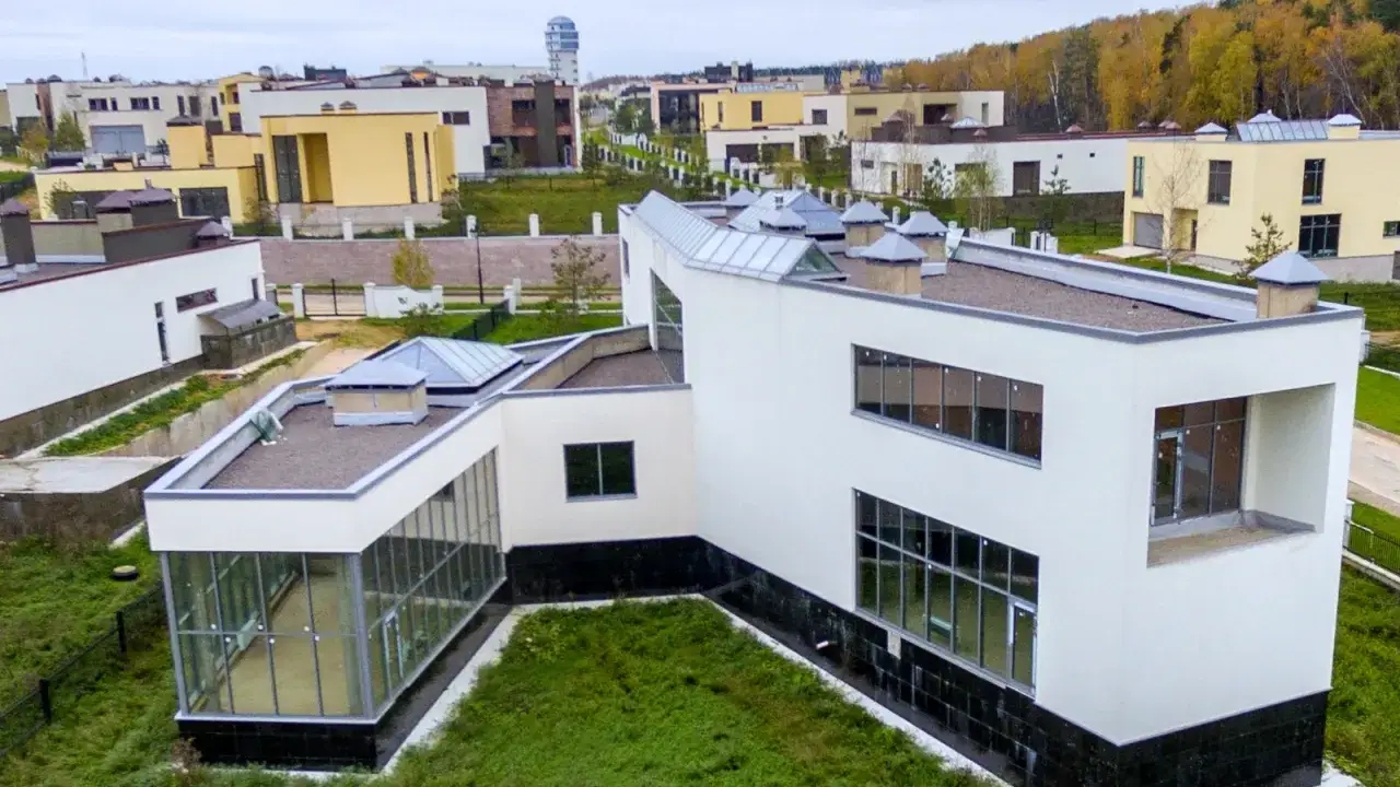 Widok z g&oacute;ry na nowoczesne budynki z płaskimi dachami, niekt&oacute;re z przeszklonymi elementami i świetlikami.