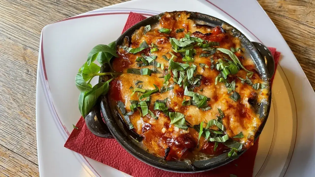 Herzhaftes Parmigiana di melanzane, überbacken mit Käse und garniert mit frischem Basilikum, serviert in einem dunklen Keramikschälchen.