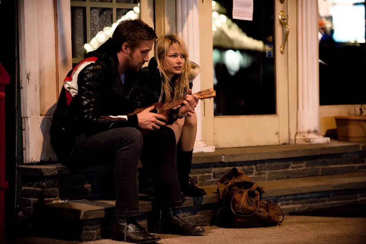 Una coppia seduta sui gradini di casa, lui suona l'ukulele. Scena che anticipa la **blue valentine trama** e le sue sfumature emotive.
