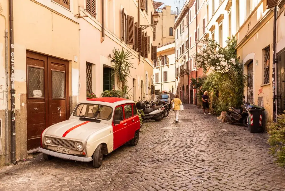 Un vicolo di Trastevere con un'auto d'epoca, scooter e persone che passeggiano. Un assaggio di cosa vedere in questo quartiere romano.
