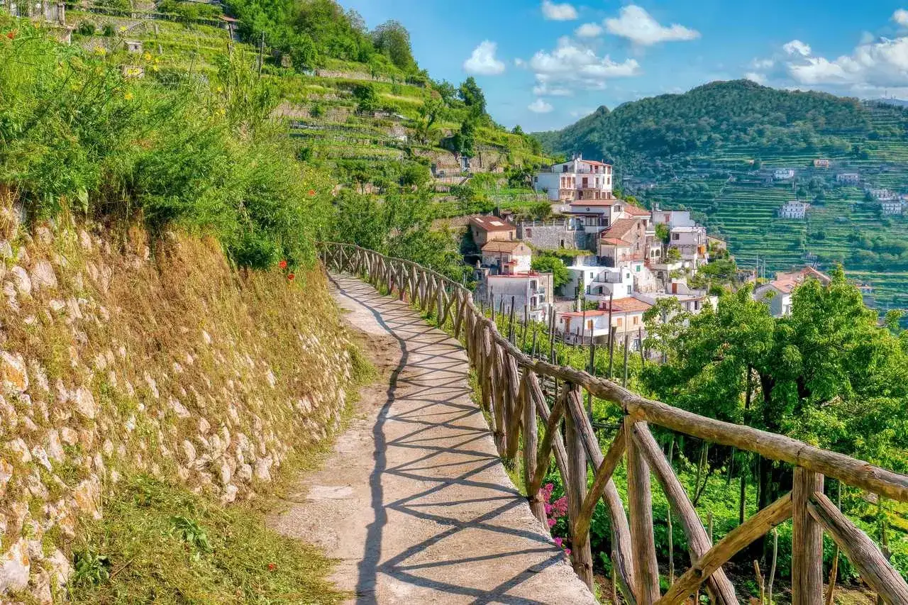 Sentier ensoleillé sur la côte Amalfitaine, menant à un village pittoresque niché sur les pentes verdoyantes. Parfait pour une randonnée mémorable.