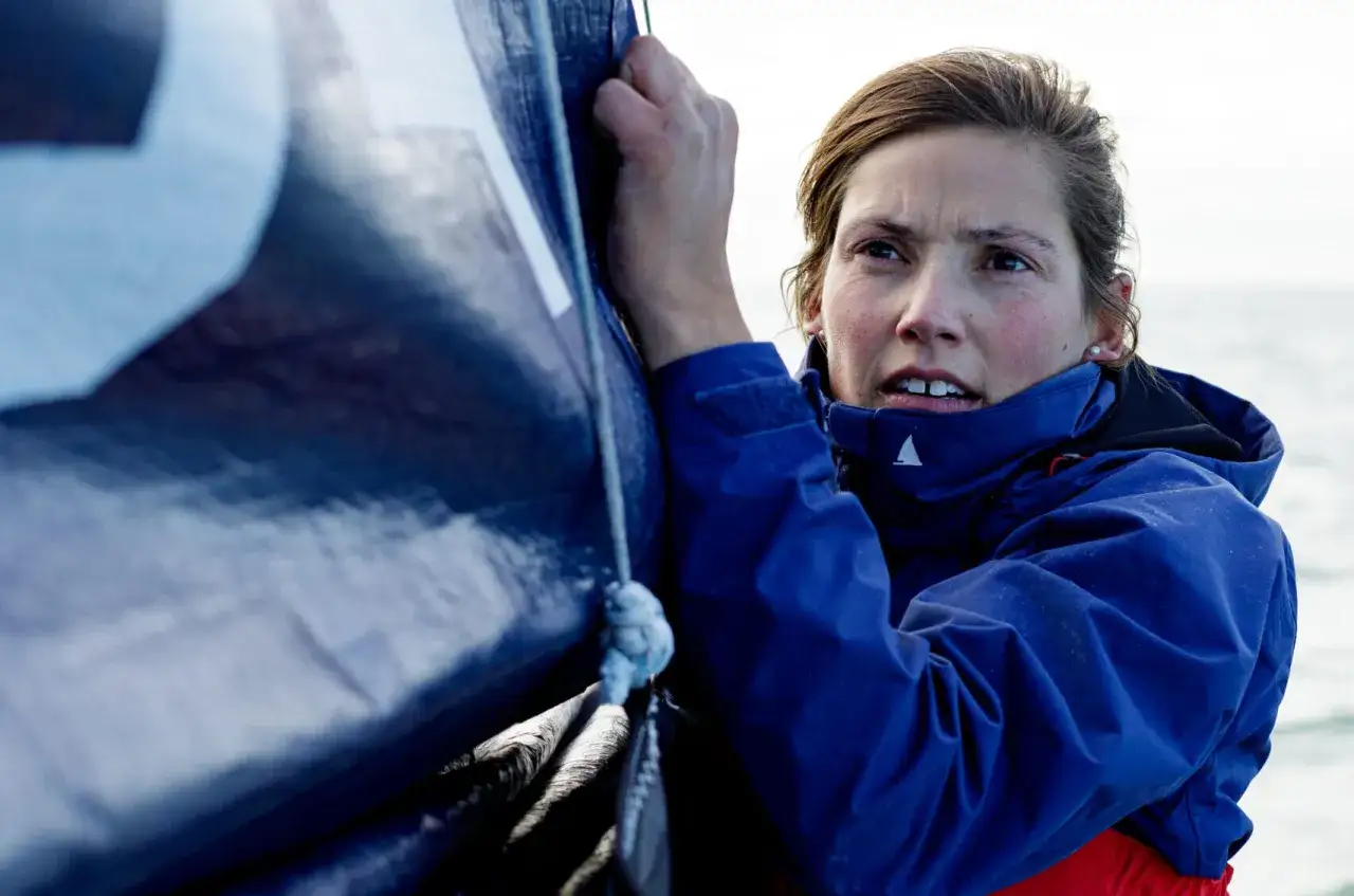 Tiphaine Ragueneau, concentr&eacute;e, ajuste une voile bleue sur un bateau. La mer est calme.