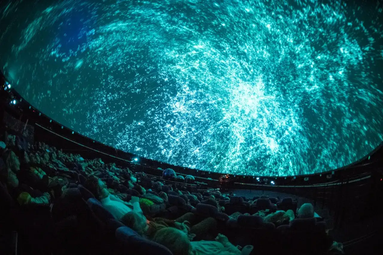 Widownia w **planetarium Warszawa** podziwia wirujący kosmos na kopule.