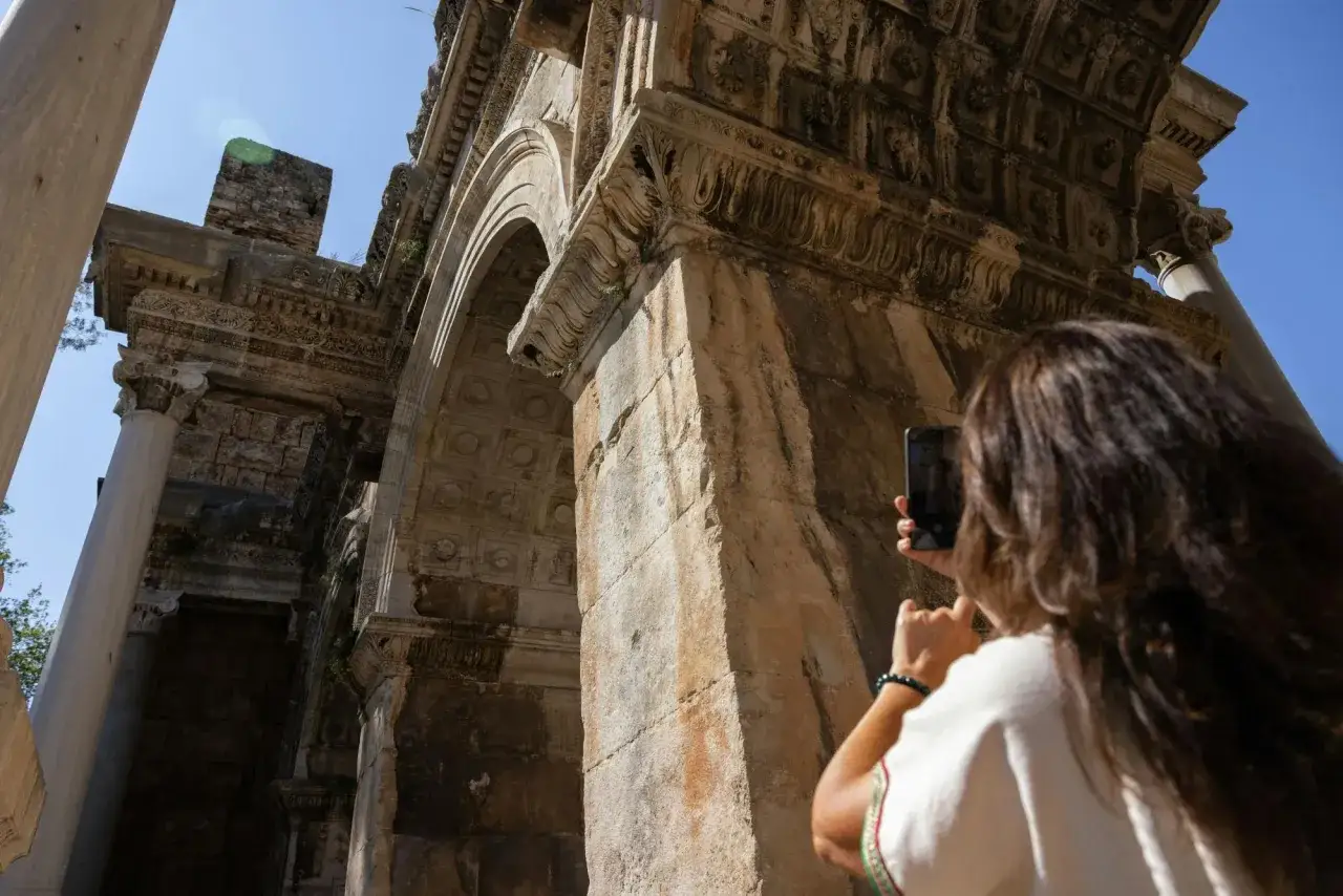 Une femme prend une photo d'une arche romaine antique. Une excellente idée pour savoir que faire à Antalya et découvrir son histoire.