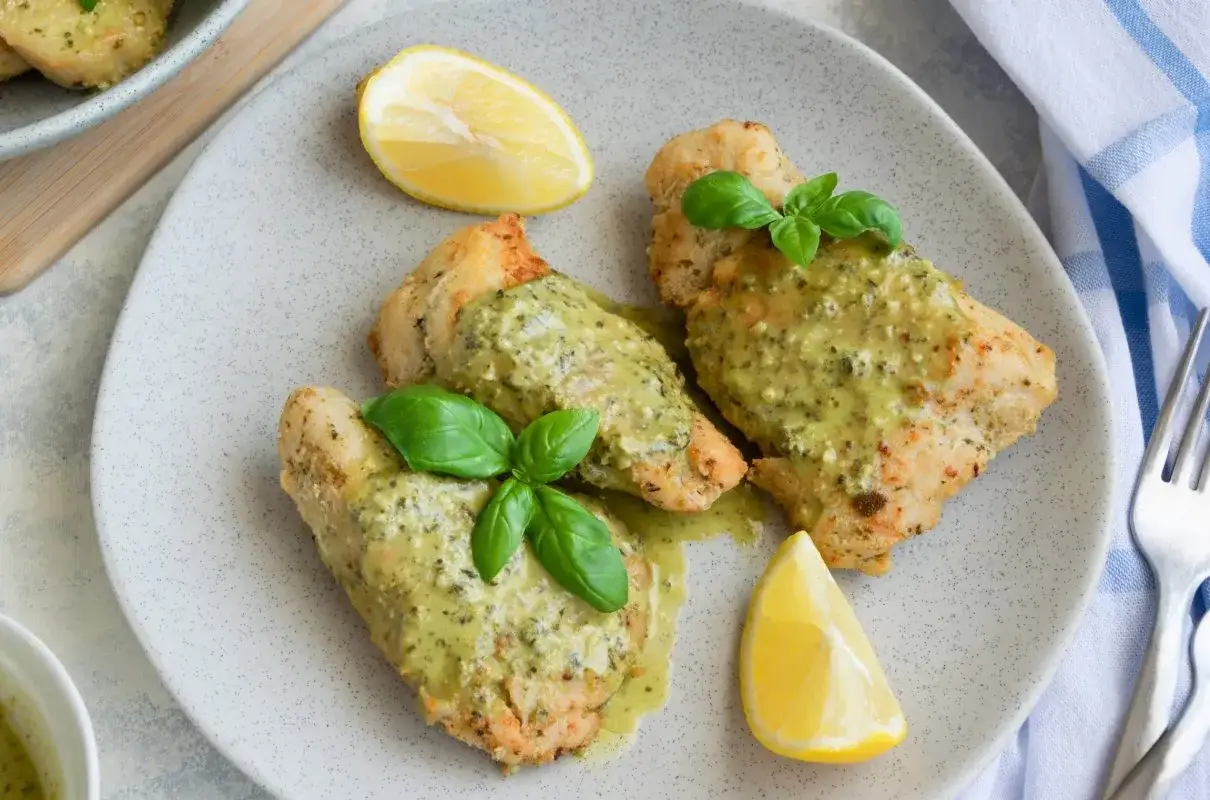 Soczysty kurczak z pesto, udekorowany listkami bazylii i kawałkami cytryny. Pyszne danie gotowe do podania.