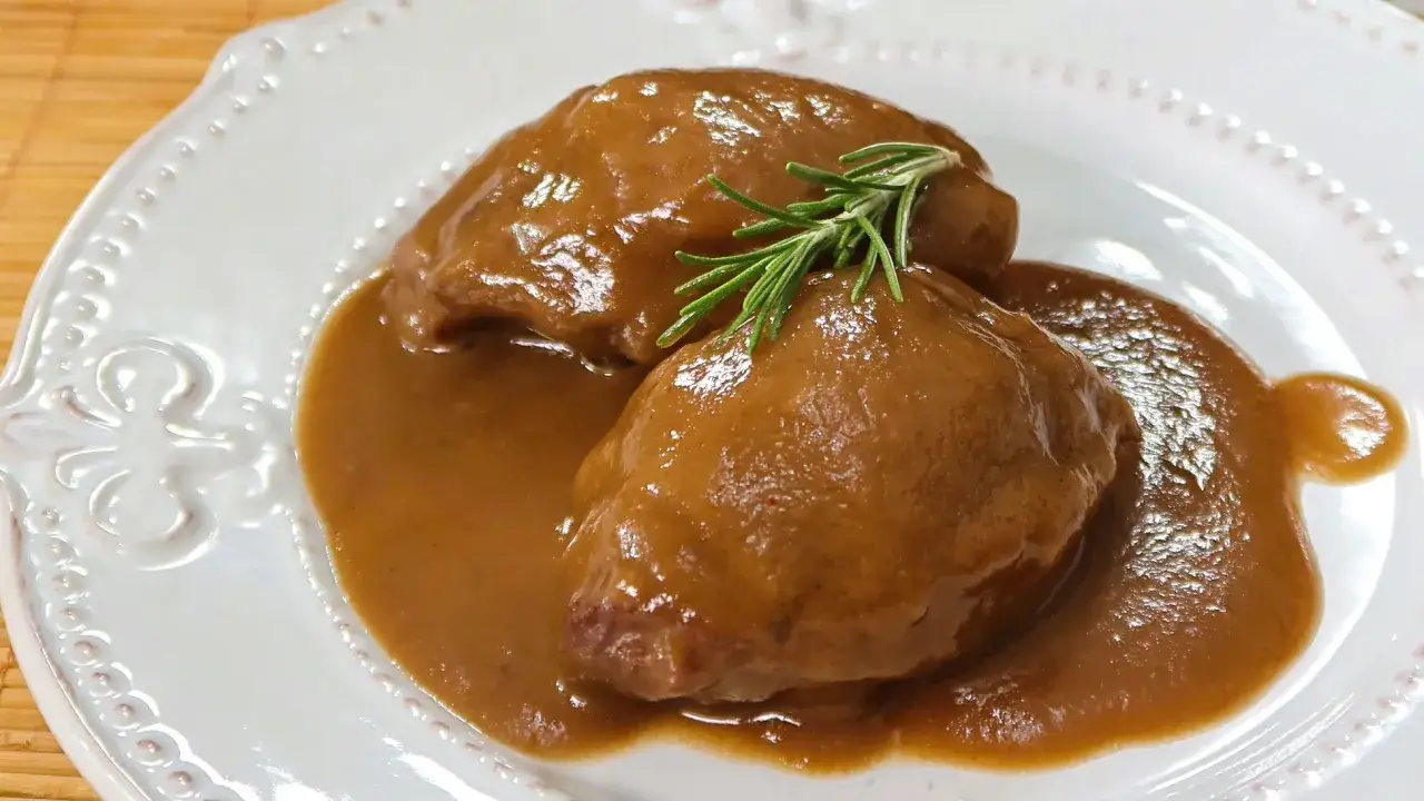 Deliciosas carrilleras de cerdo estofadas en salsa, coronadas con romero fresco.
