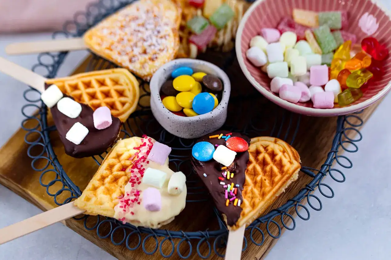 Herzförmige Waffeln am Stiel, dekoriert mit Schokolade, Marshmallows und Streuseln. Ein süßes Rezept für Waffeln am Stiel!