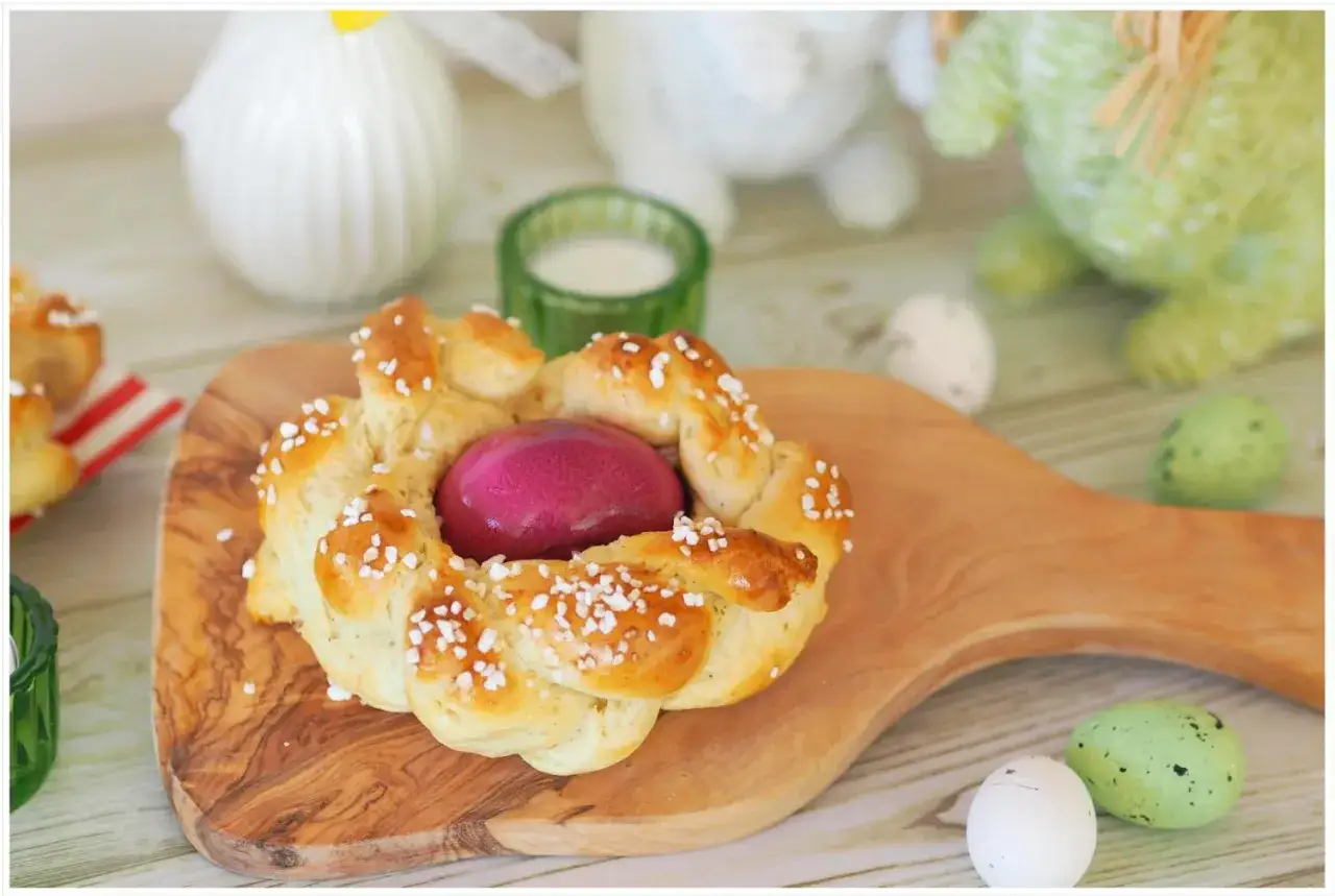 Ein geflochtener Osterkranz mit einem lila Ei in der Mitte, bestreut mit Zuckerperlen. Ein tolles Osterkuchen Rezept für die Feiertage.