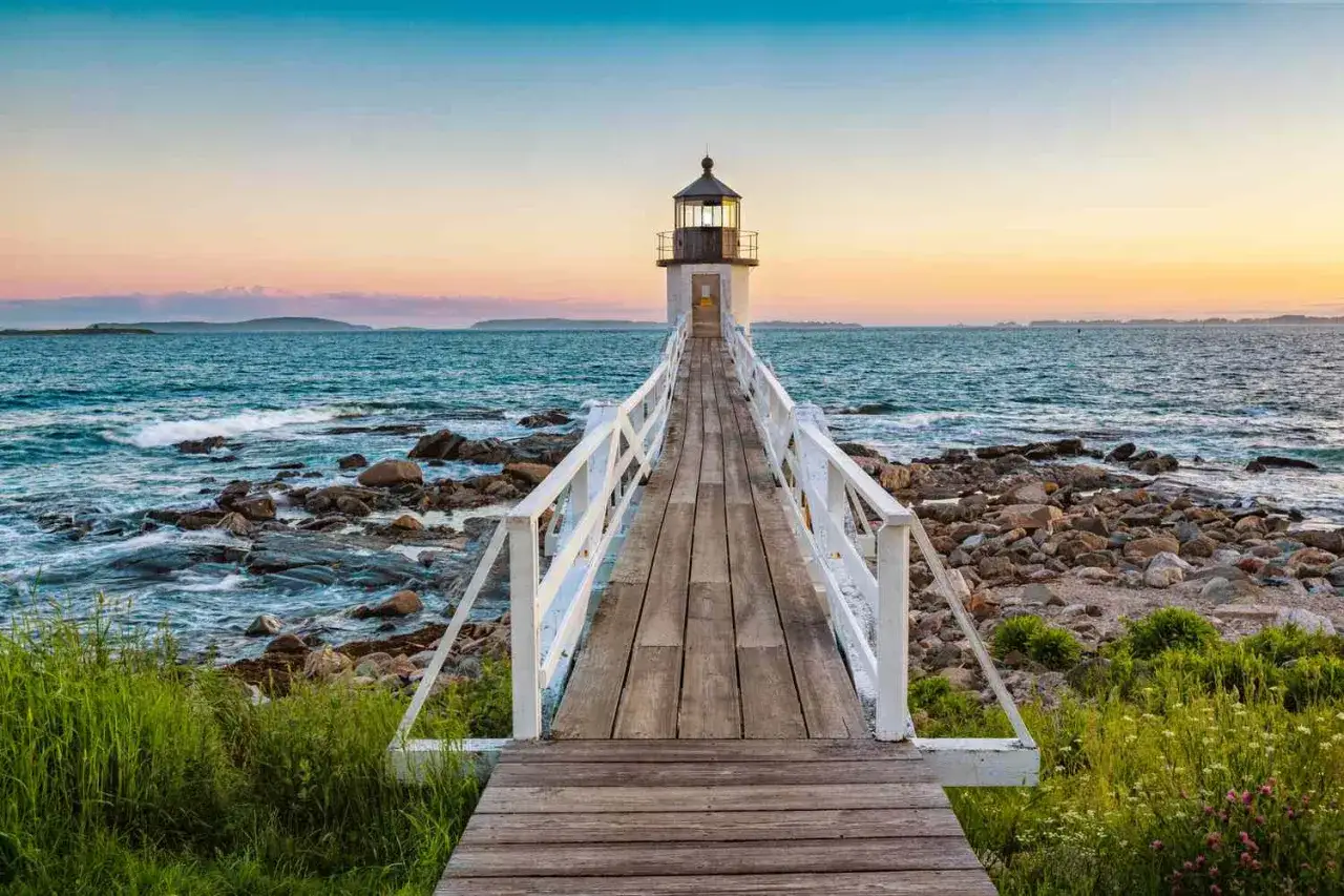 Holzsteg f&uuml;hrt zu einem Leuchtturm am Meer. Perfekte reiseziele august f&uuml;r Ruhe und Ausblick.