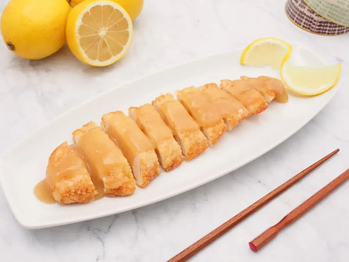 Tiernas lagrimitas de pollo ba&ntilde;adas en salsa, acompa&ntilde;adas de limones frescos y palillos.