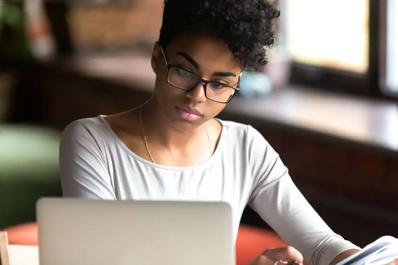 Junge Frau mit Brille konzentriert sich auf ihren Laptop, w&auml;hrend sie Dokumente pr&uuml;ft. Sie arbeitet an ihrem **iu modemanagement**.