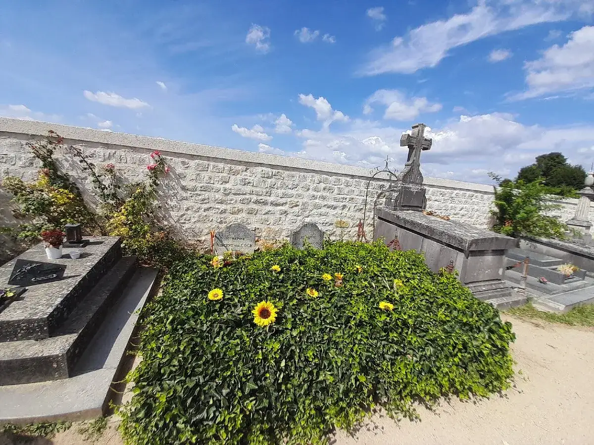 Le tombeau de Van Gogh, couvert de verdure et de tournesols, sous un ciel bleu.