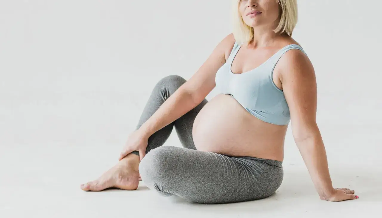 Gravid kvinna sitter på golvet, håller om sitt ben som känns ont.
