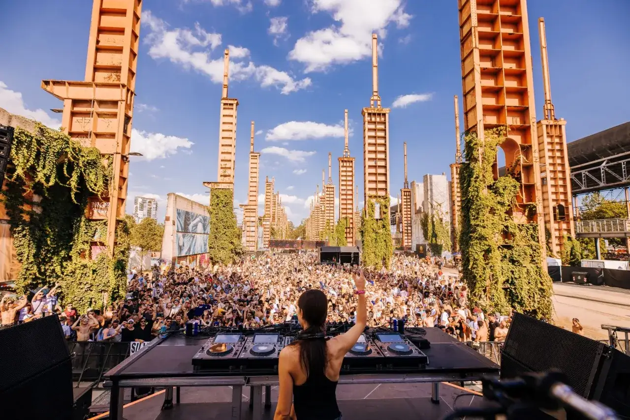 DJ al **Futur Festival Torino** saluta la folla sotto torri arrugginite e cielo azzurro. Musica e energia in un'ambientazione unica.
