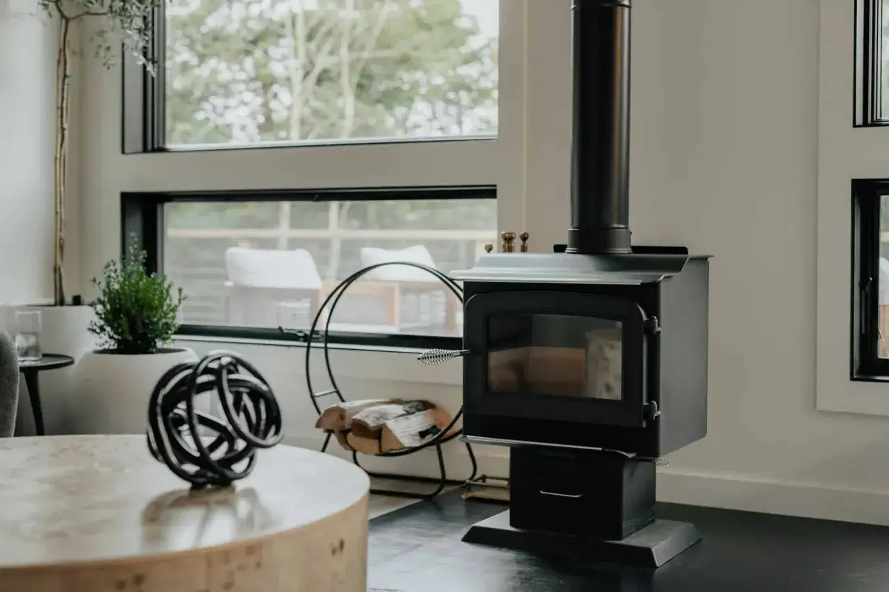 Poêle moderne en fonte, prêt à réchauffer le salon. Bois empilé à proximité, invitant à la détente.