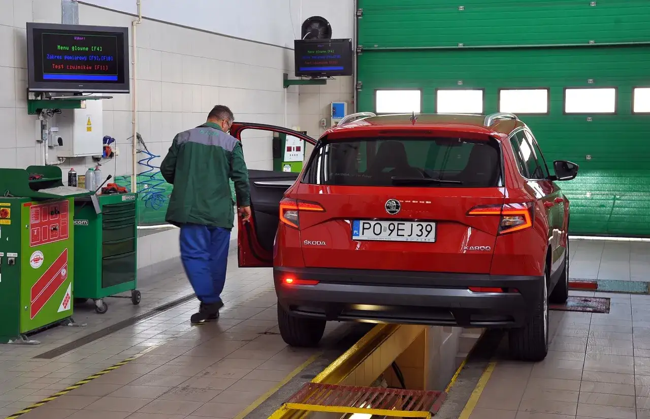 Pracownik serwisu sprawdza czerwonego Skodę Karoq. Na ekranie widać menu diagnostyczne, co może pomóc ustalić, ile kosztuje przegląd techniczny samochodu.