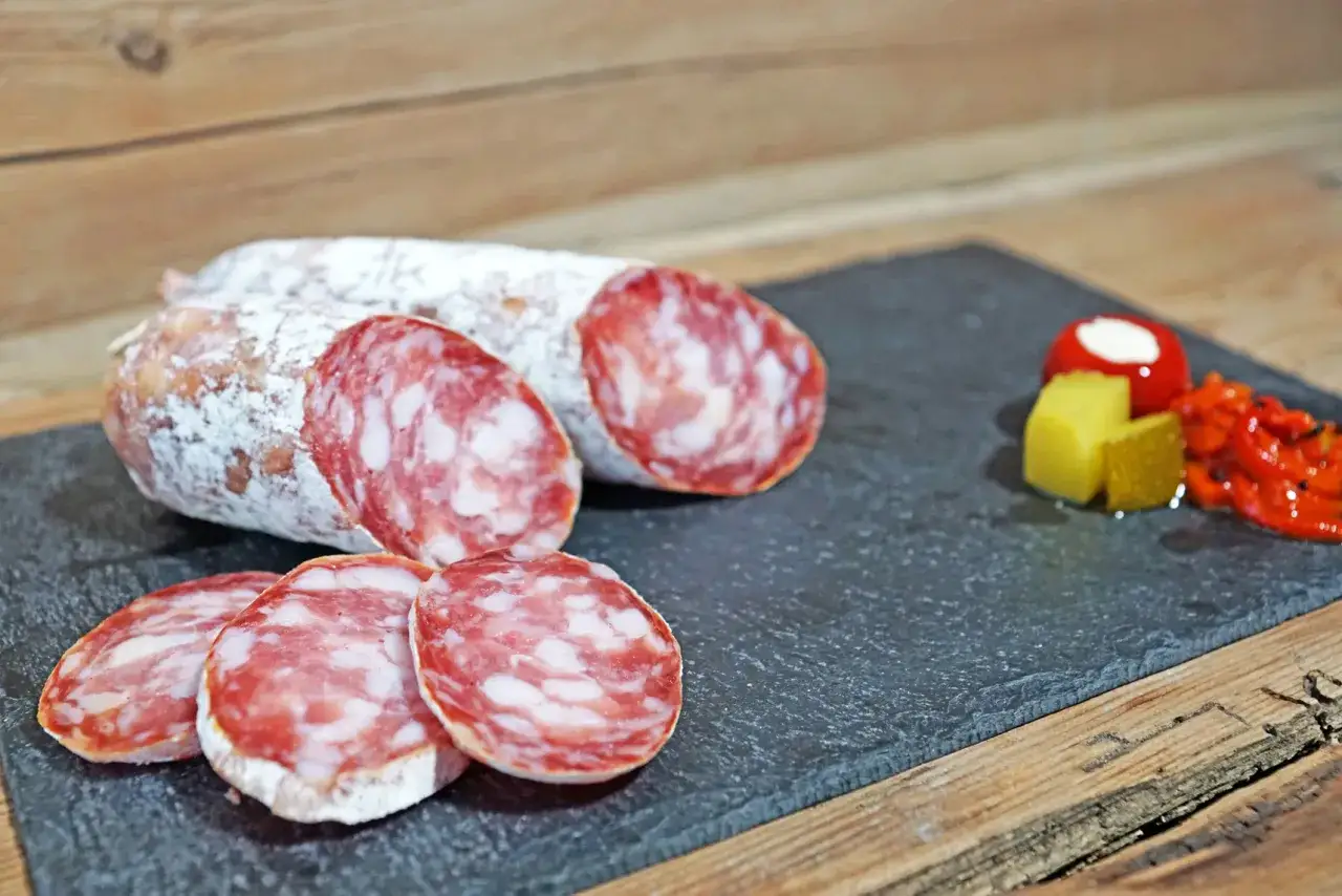 Tranché, le saucisson sec se présente sur une ardoise avec des poivrons grillés. Peut on cuire du saucisson sec ? Non, il est déjà prêt à déguster.