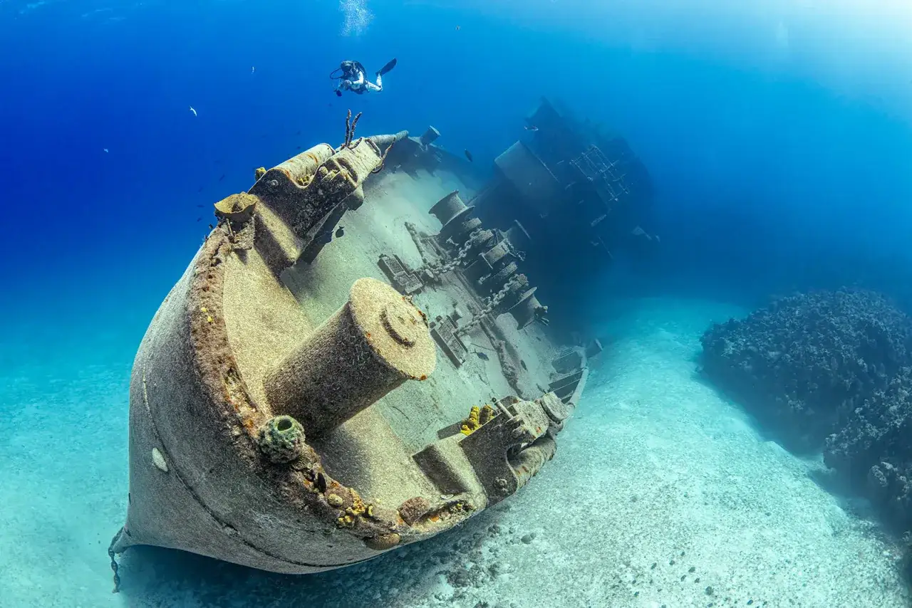 Plongée dans les profondeurs bleues, une photographie sous-marine révèle une épave de navire, vestige d'une histoire oubliée, où un plongeur explore ce monde silencieux.