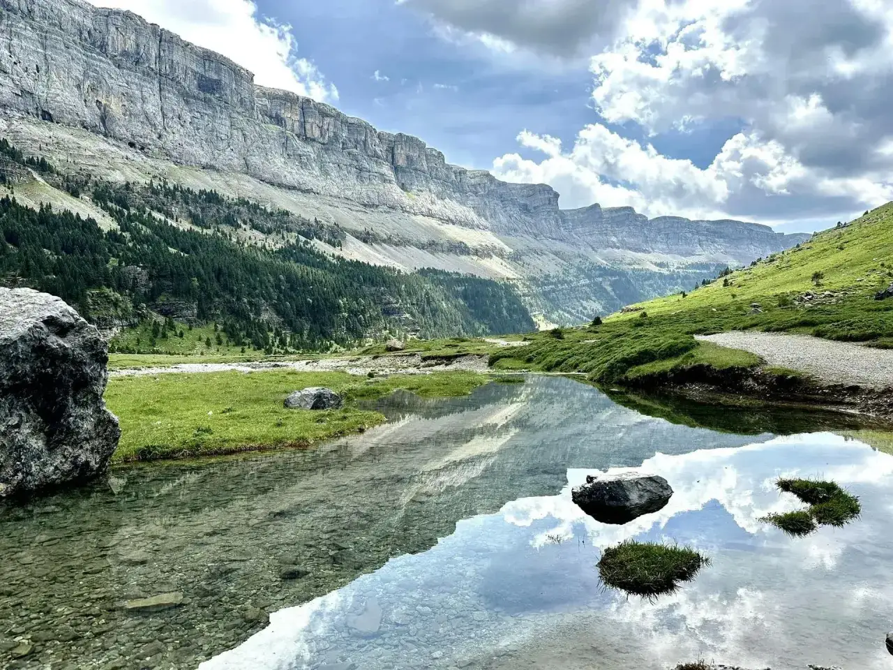 Un lago sereno refleja las imponentes paredes rocosas y los bosques verdes de los montes Pirineos.