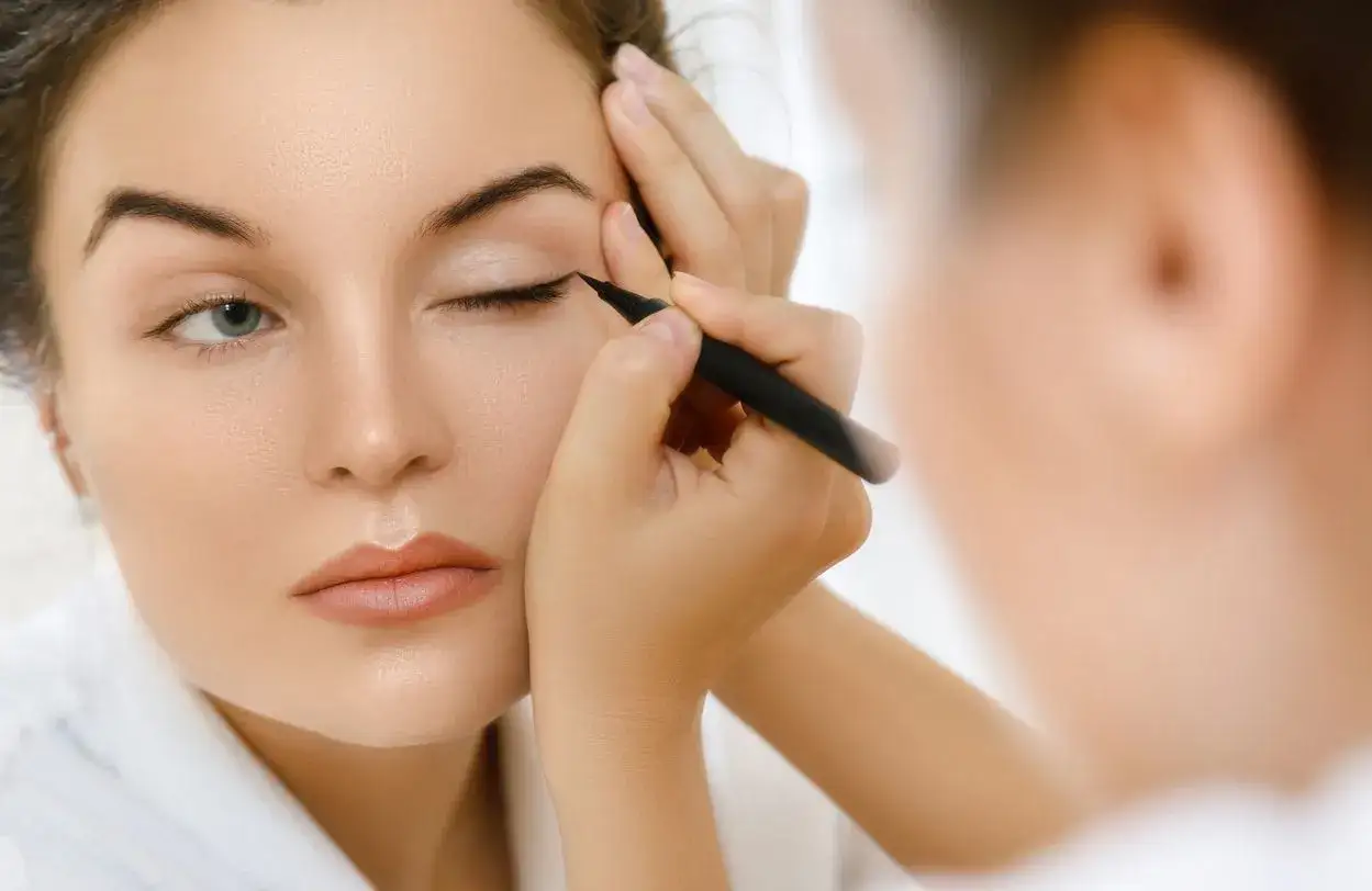 Une femme applique un trait d'eye-liner pour un maquillage pour agrandir les yeux. Son regard est intense, pr&ecirc;t &agrave; conqu&eacute;rir le monde.
