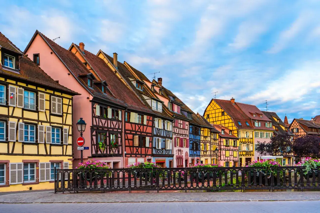 Maison alsacienne avec une fa&ccedil;ade color&eacute;e, des colombages et des toits en tuiles rouges, sous un ciel bleu.