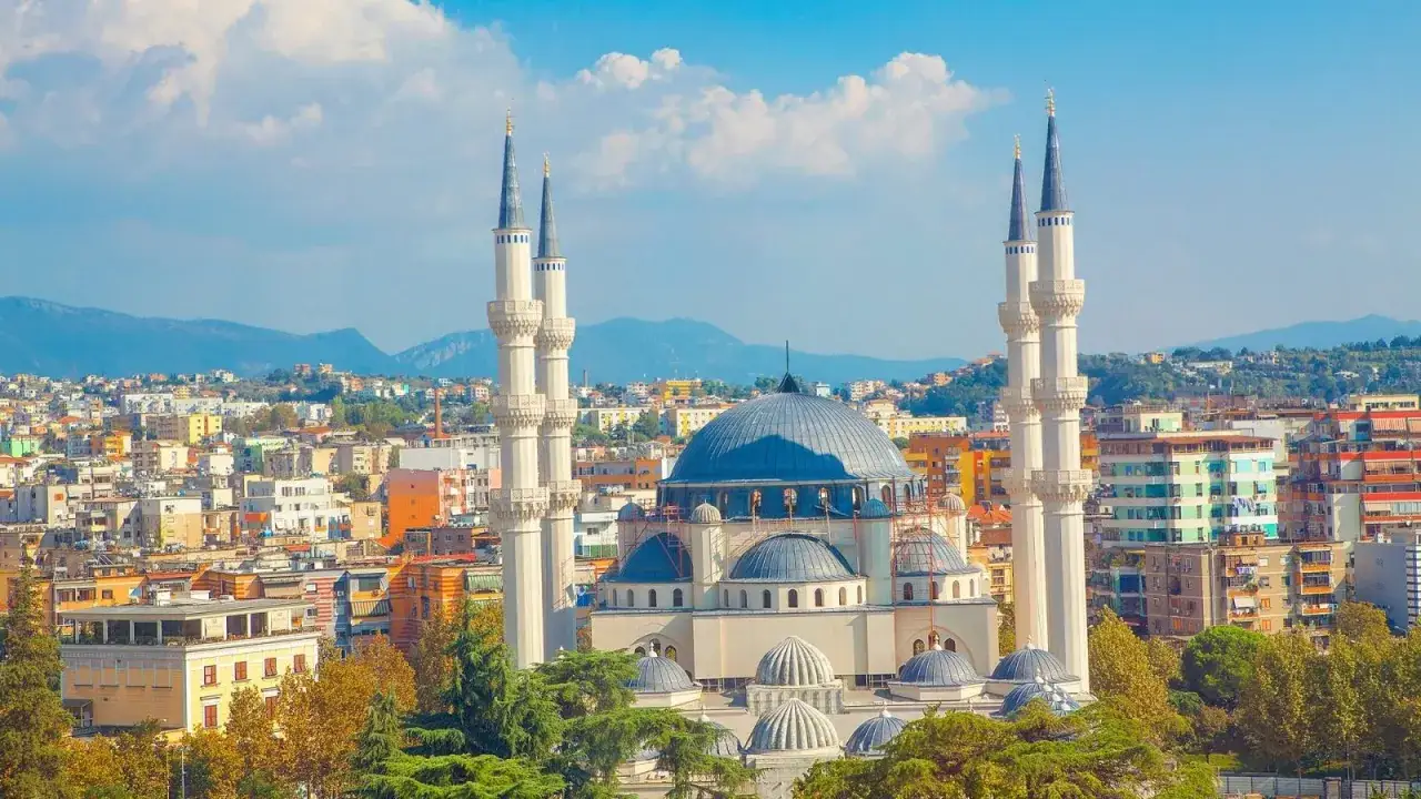 Imponująca panorama miasta, gdzie w centrum wznosi się wielka, błękitna kopuła meczetu. To serce **Albania stolica**, otoczone kolorowymi budynkami i zielenią.