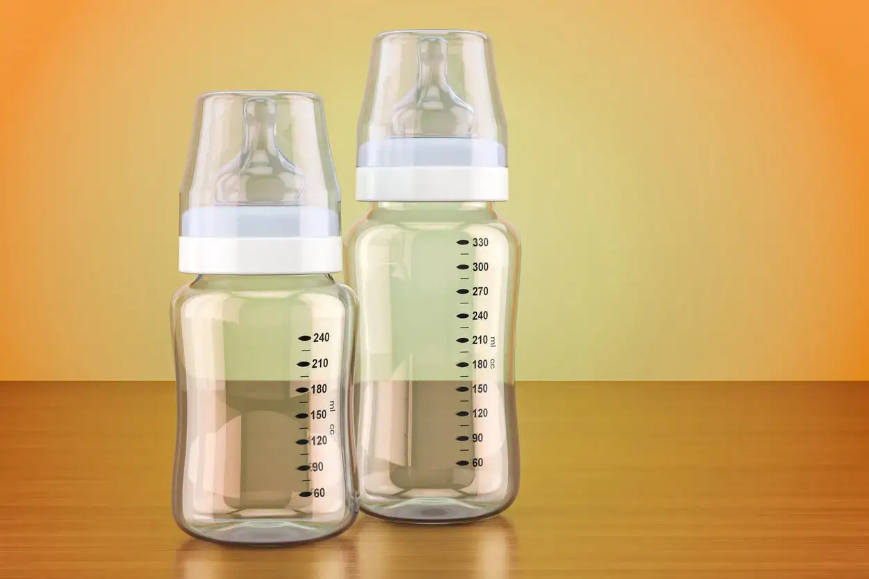 Dos biberones, uno de cristal o plástico más pequeño y otro más grande, con marcas de medición.