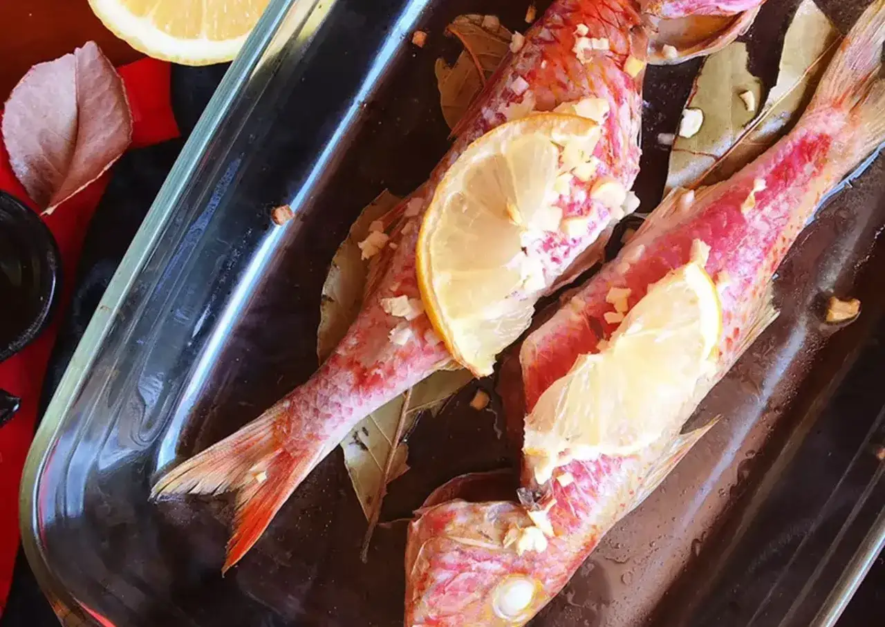 Dos salmonetes al horno, listos para cocinar con rodajas de lim&oacute;n y ajo.