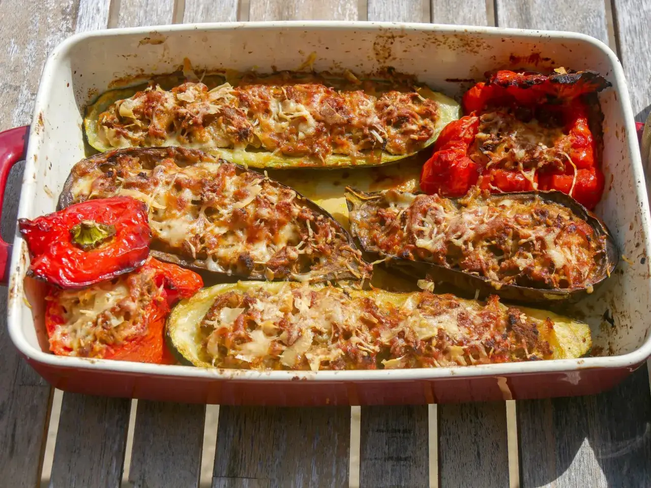 Plat de petits farcis aux légumes, courgettes, aubergines et poivrons rouges, gratinés au fromage, prêts à être dégustés.