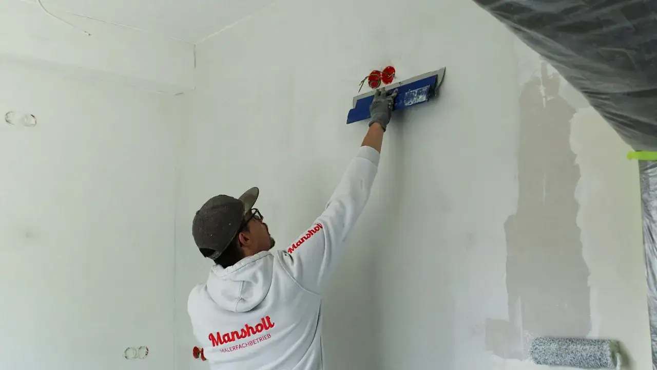 Maler spachtelt Rigips-Wand glatt. Mit einem breiten Spachtel werden Unebenheiten ausgeglichen, um eine perfekte Oberfl&auml;che f&uuml;r die weitere Bearbeitung zu schaffen.