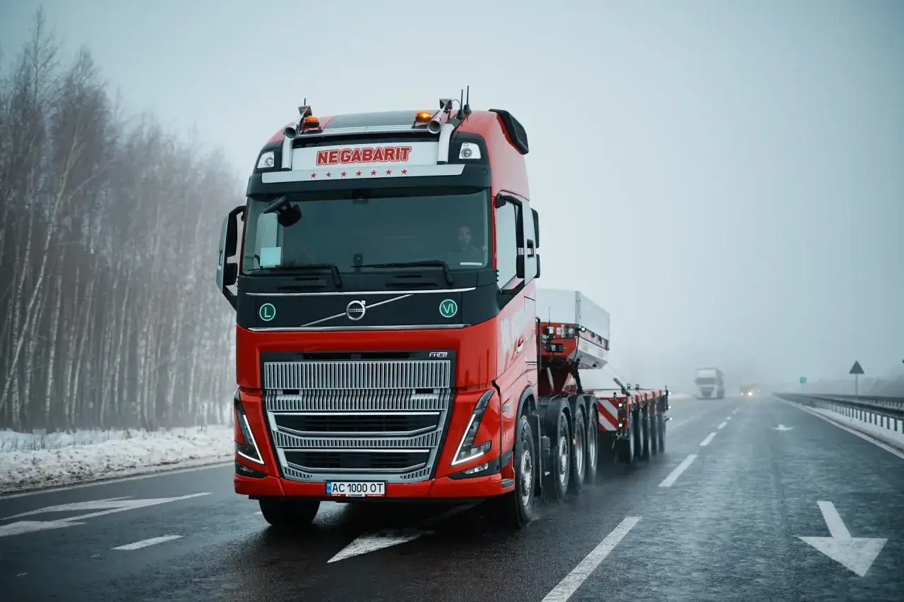 Czerwony Volvo FH16 z naczepą jedzie po mokrej drodze w mglisty dzień.